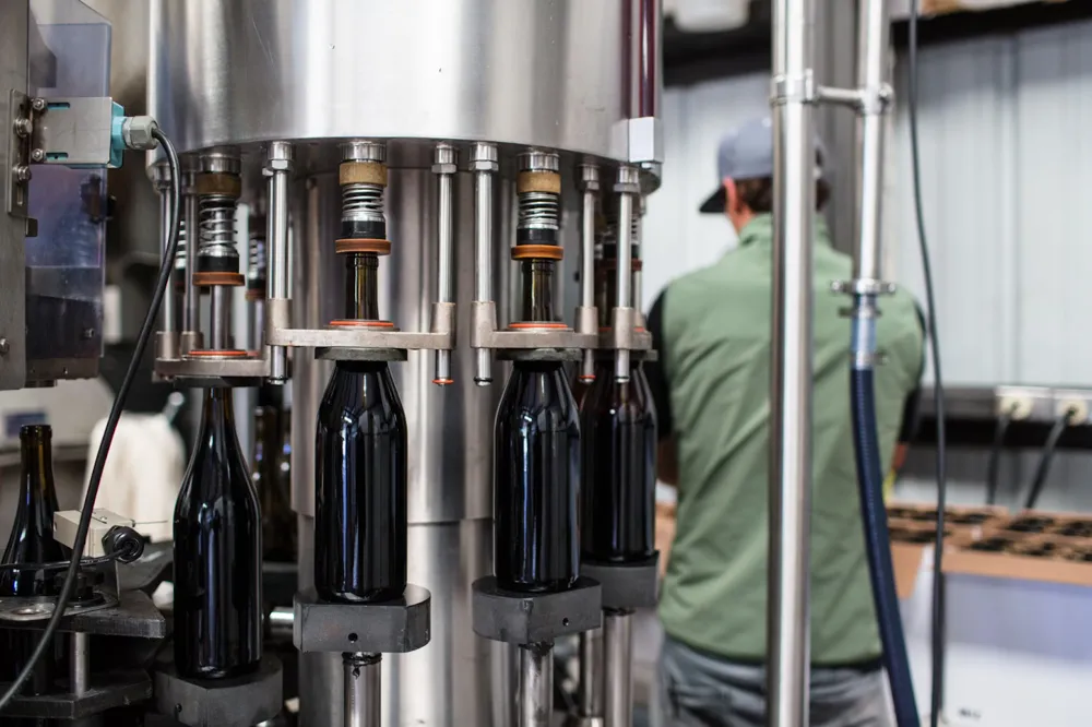 Automatic bottling lines limit human error and ensure consistency in each bottle (Photo by<a href="https://unsplash.com/@vindemia?utm_content=creditCopyText&amp;utm_medium=referral&amp;utm_source=unsplash"> Vindemia Winery</a> on<a href="https://unsplash.com/photos/black-glass-bottles-on-stainless-steel-rack-OQ_o-SaEMiI?utm_content=creditCopyText&amp;utm_medium=referral&amp;utm_source=unsplash"> Unsplash</a>)